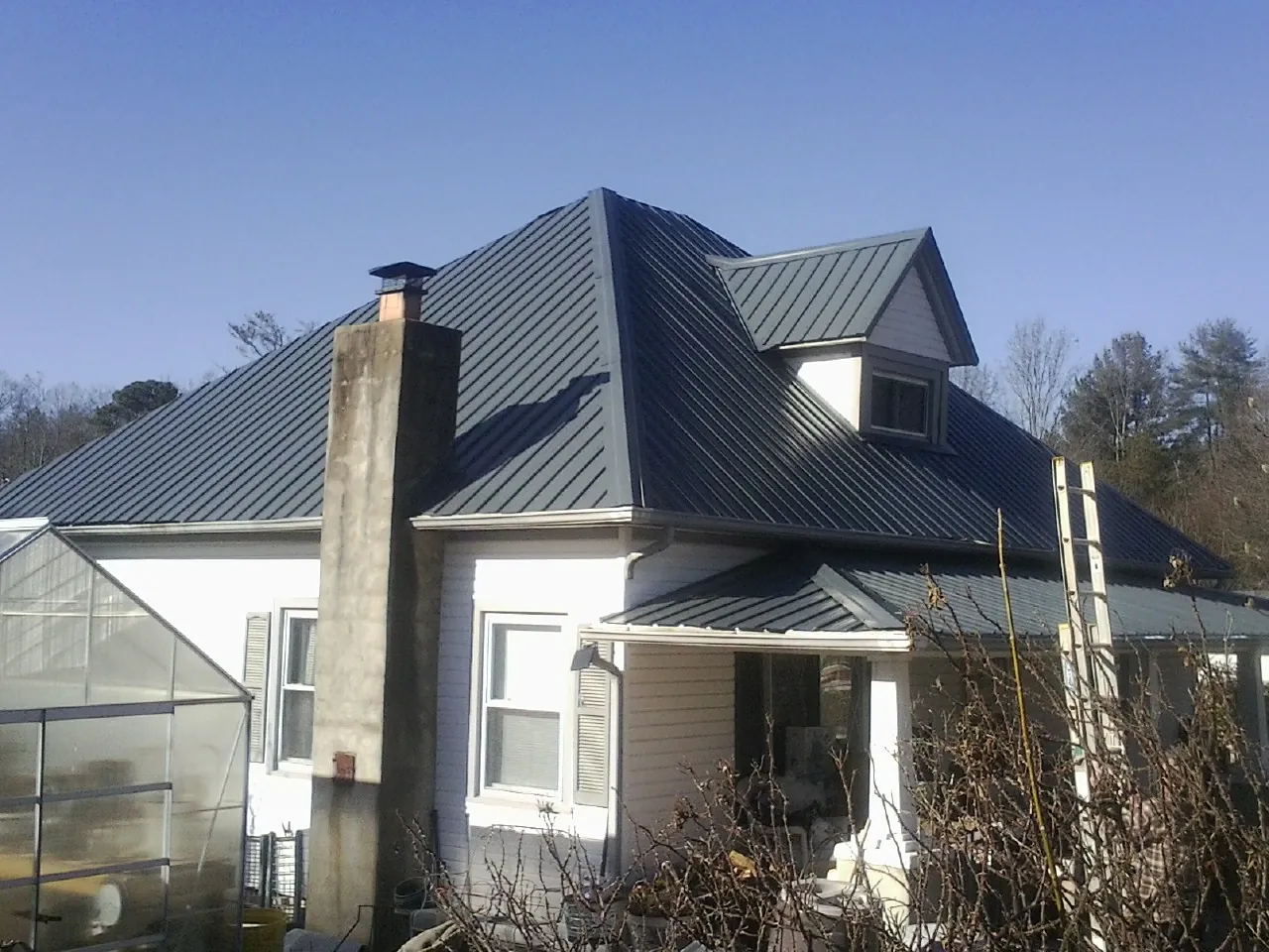 Dark blue standing seam metal roof on a white farmhouse with dormer — Slate & Tile Roof Repair by Roofing Brothers in Long Beach