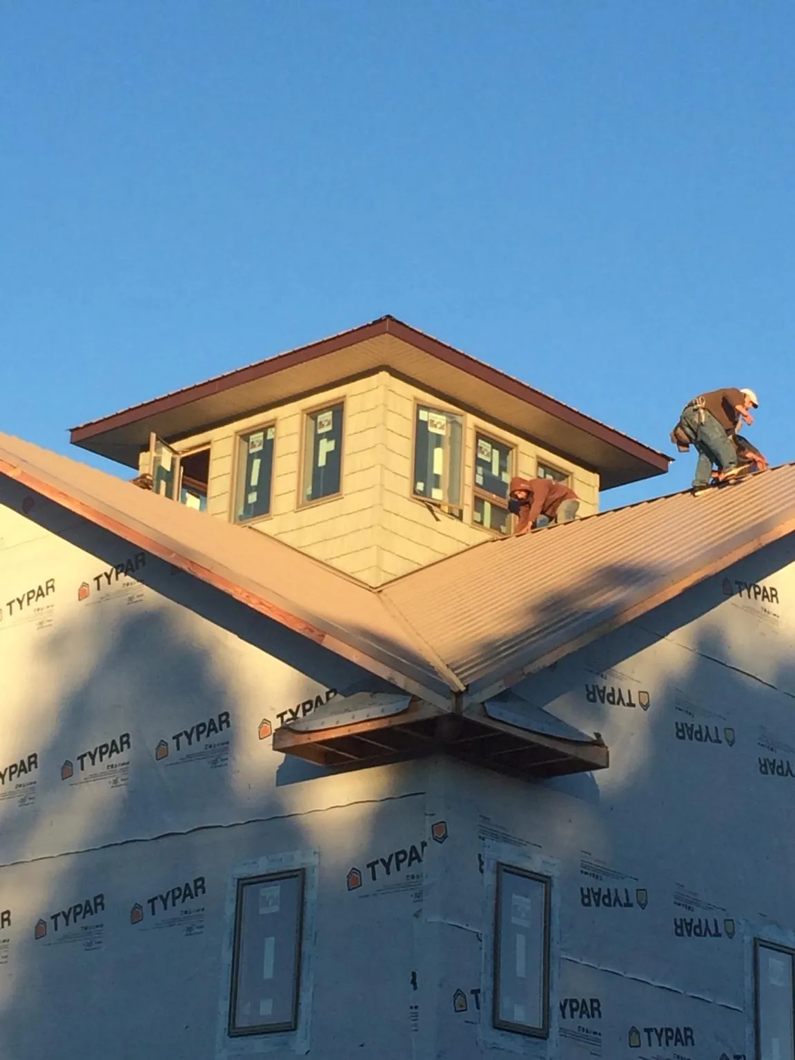 Roofers working around a rooftop cupola on a new metal roof at sunset in Long Beach